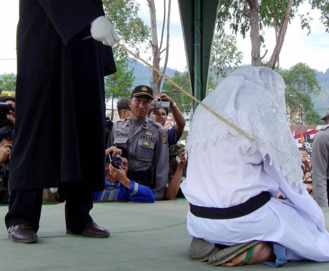 TAKENGON, INDONESIA: An Acehnese executor flogs a convicted woman in Takengon, in Indonesian central Aceh province, 19 August 2005 after an Islamic sharia court ordered four women to be flogged for petty gambling offences. The public lashing was the second since the Indonesian government allowed the western province to implement religious law as part of broader autonomy granted in 2001 to curb a separatist Islamist insurgency. AFP PHOTO (Photo credit should read STR/AFP/Getty Images)