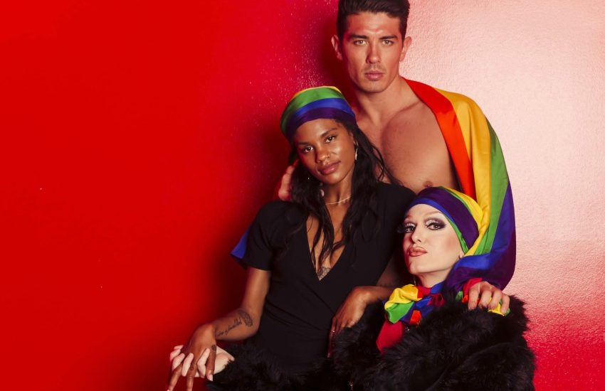 Three models standing behind each other with pride scarves against a red wall