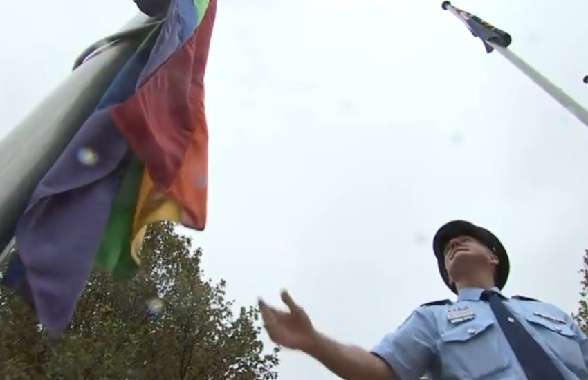 A police officer watches as the rainbow flag goes up a flag pole