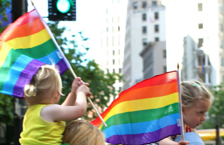 Two girls sit on their parents shoulders at Pride event