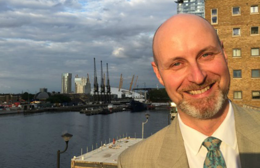 Phil Nicol in a suit smiling in front of the Thames River