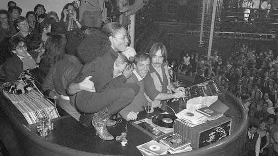 Black and White photo. a lady is standing on dj decks while people below her look up and smile