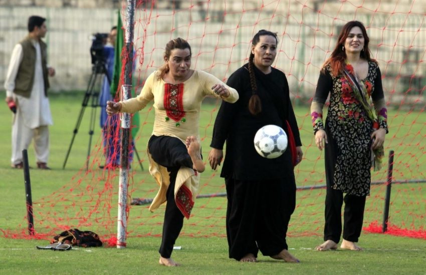 a woman kicking a soccer ball as two other women look on