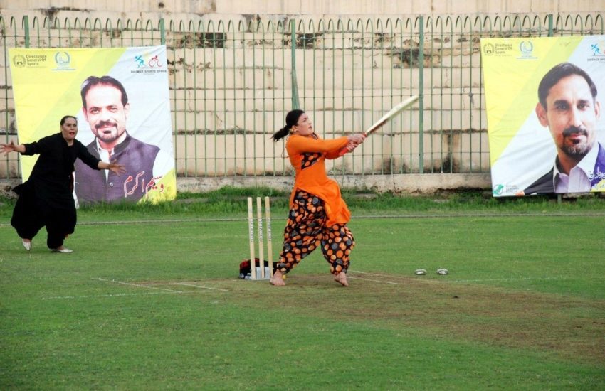 A woman at a cricket wicket hitting a ball with a cricket bat, she's wearing orange