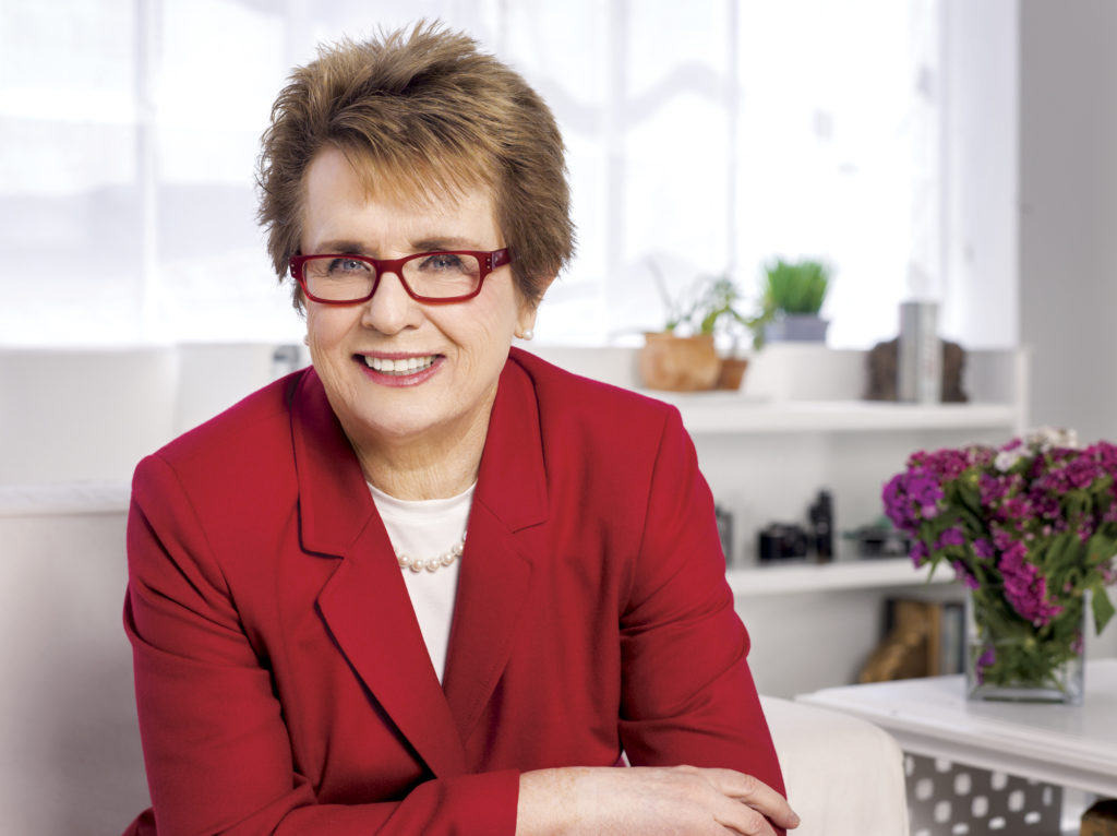 Billie Jean King wearing a red jacket while sitting at a table