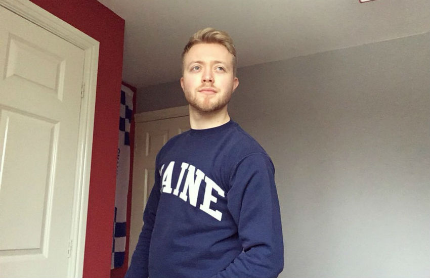 Chris standing in his room wearing a jumper