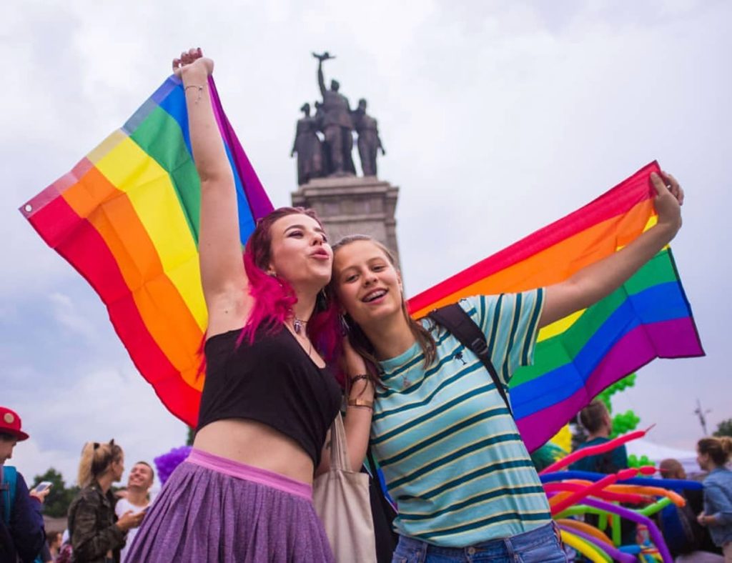 Two girls waving the rainbow flag at Sofia Pride.