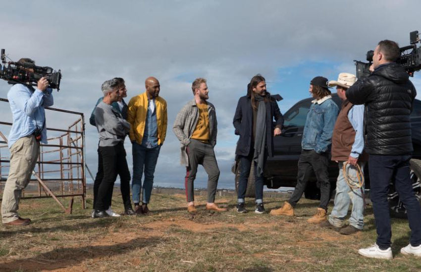 the five queer eye guys standing outside talking to two men who are standing front of a vehicle on a farm, on either side of them are two people with video cameras filming them