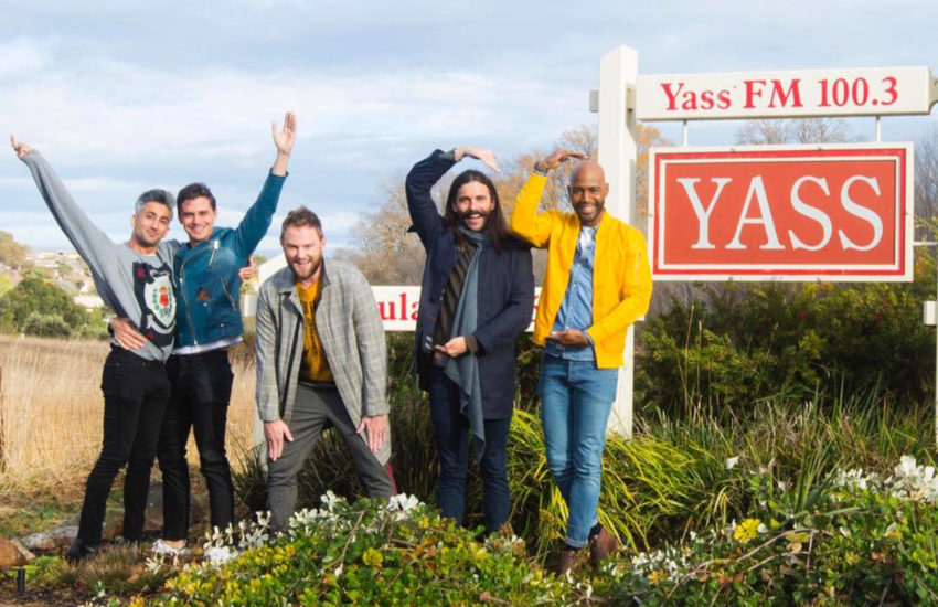 The fab five spelling out the letters of yass with their bodies and standing next to a sign that writes yass