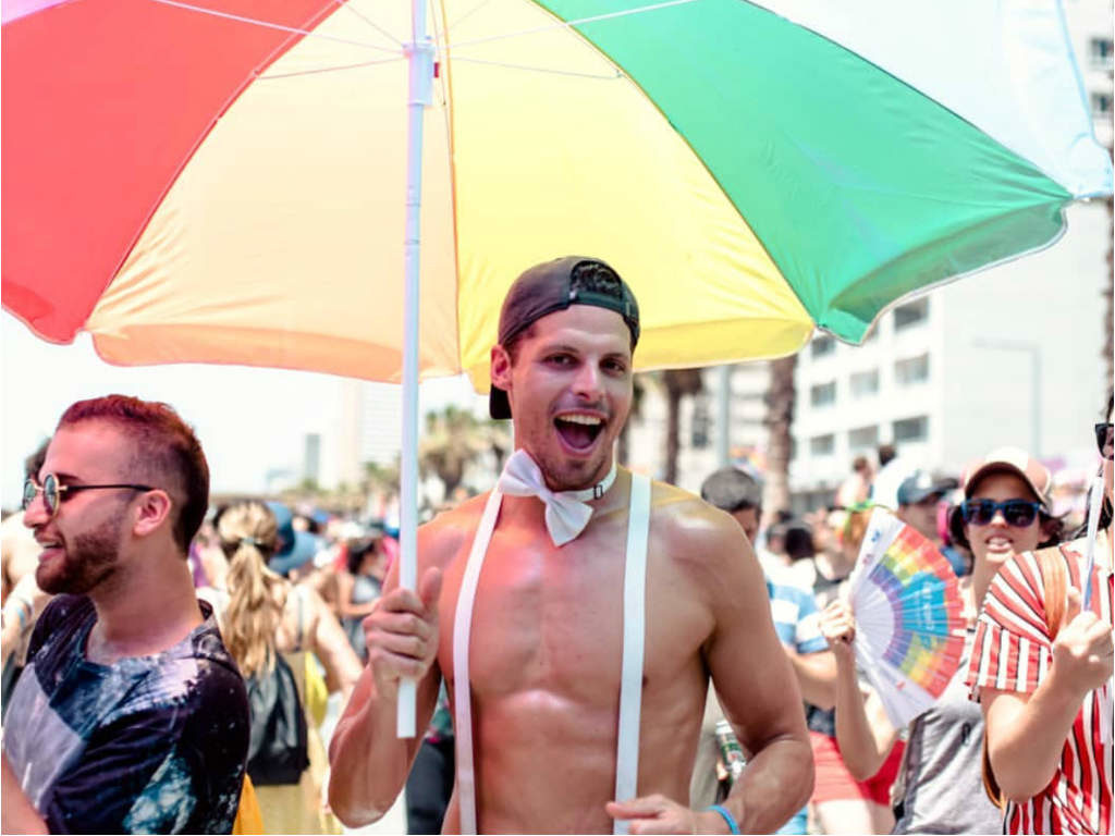 A guy holding a rainbow beach umbrella