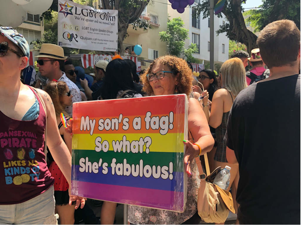 A woman holding a sign 'My son's a fag! So what? She's fabulous!'