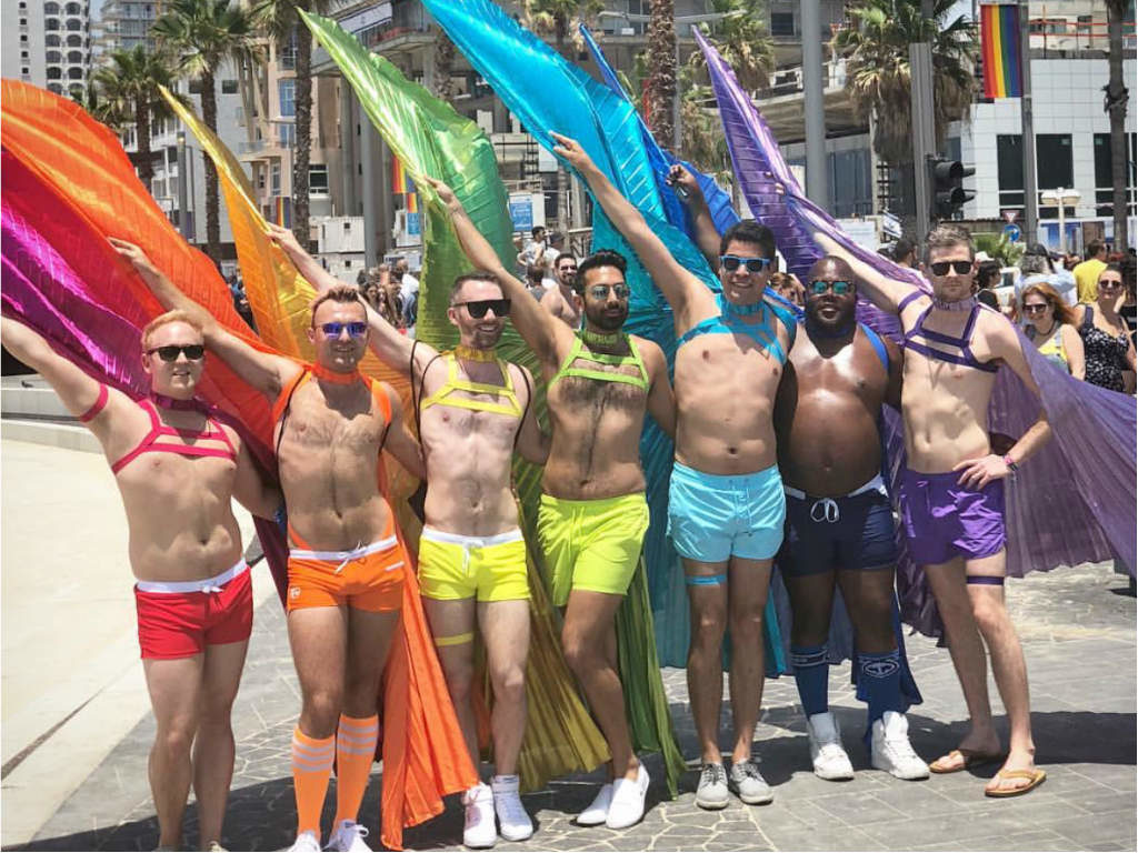 Seven men posing in rainbow costumes at Tel Aviv Pride.