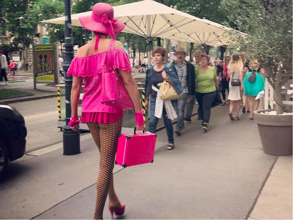 A drag queen in a pink outfit walking down the street during Vienna Pride