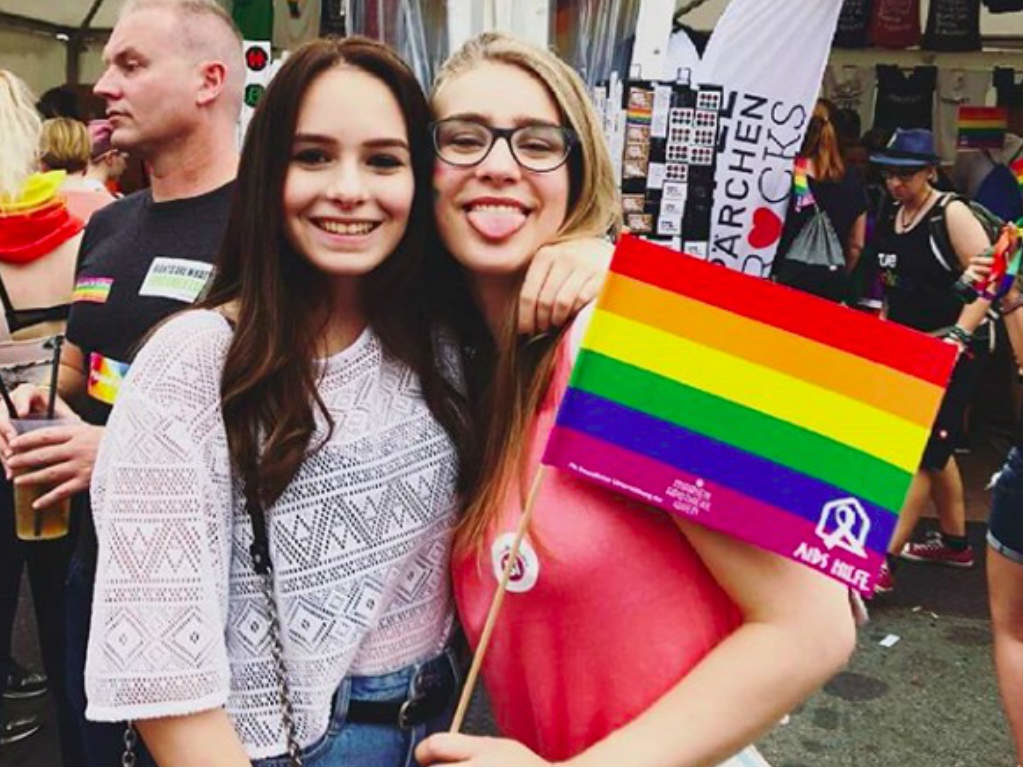 Two girls hugging while holding the rainbow flag