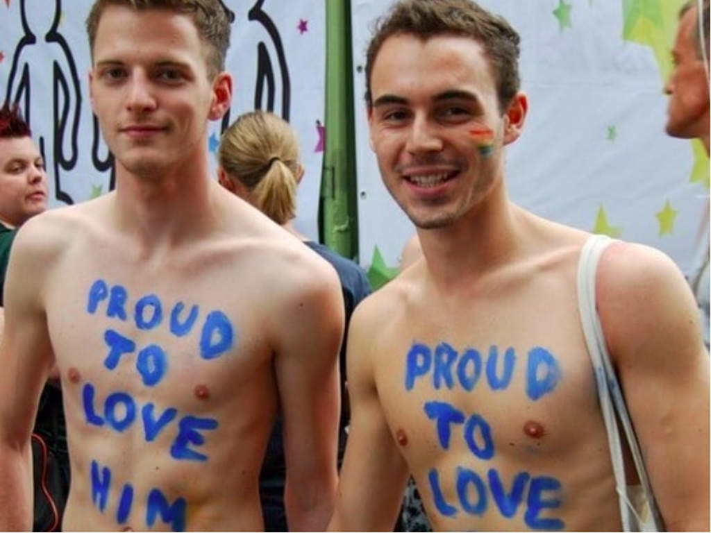 A gay couple marching at the parade. They have a 'proud to love him' writing on their bare chests.