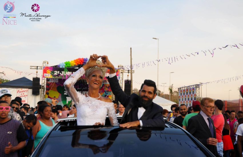 A couple standing up in the sunroof of a luxury car making a love heart sign with their hands 