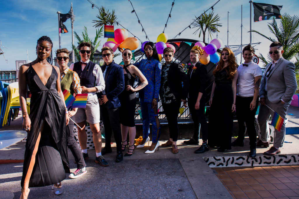 A group of people identifying as LGBTI posing for a promo shot for Queer Prom in suits and gowns.