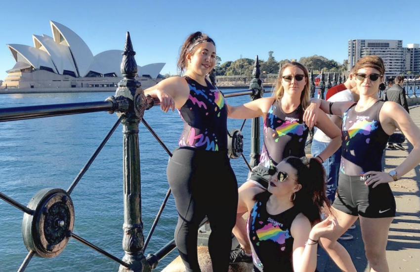 women standing in swimwear against a fence on a sunny day the sydney opera house is in the background
