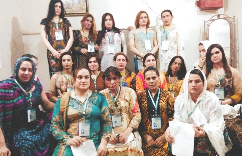 A group of women in traditional pakistan costume sit in a group they all have matching green lanyards on