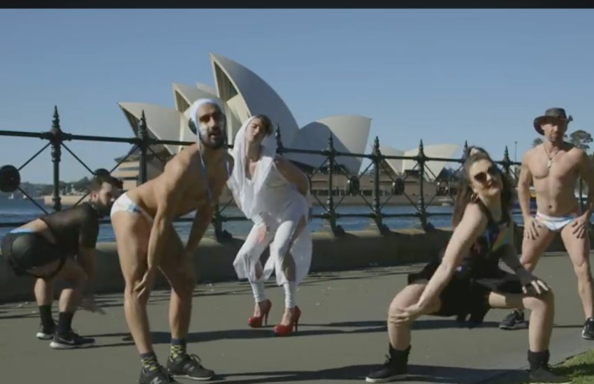 six people posing is sexy poses with sydney opera house in the background, it is a sunny day. one person is dressed as a leather daddy, two are wearing water polo swimwear, one is wearing the white costume from kylie minogue's can't get you out of my head video and one is wearing an akubra hat