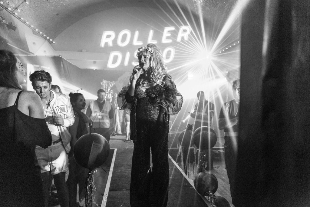 Amy Zing hosting a roller disco event where Daniel is among the crowd.