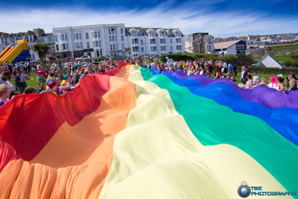A panoramic shot of people waving a giant rainbow flag.