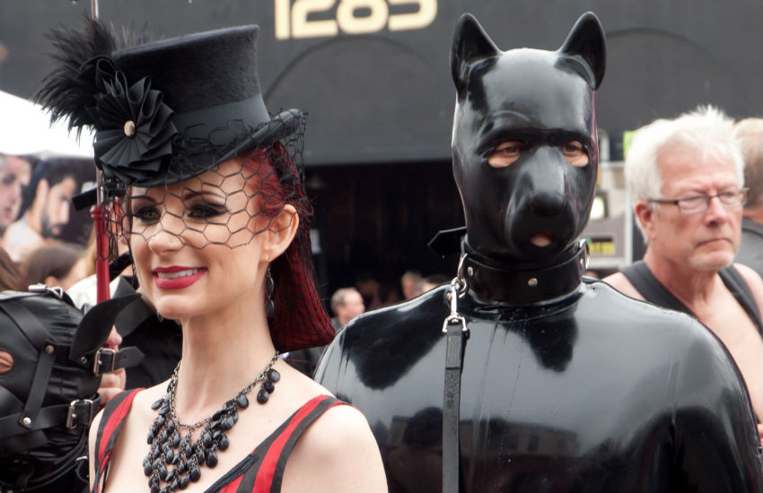 Woman dressed up in top hat with man in full leather pup suit