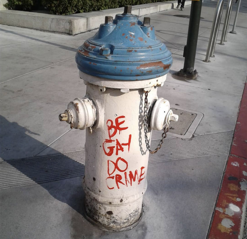 A fire hydrant graffitied with the Be Gay, Do Crime slogan 