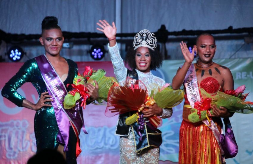 three women in glamourous gowns stand on stage holding flowers and waving to the crowd