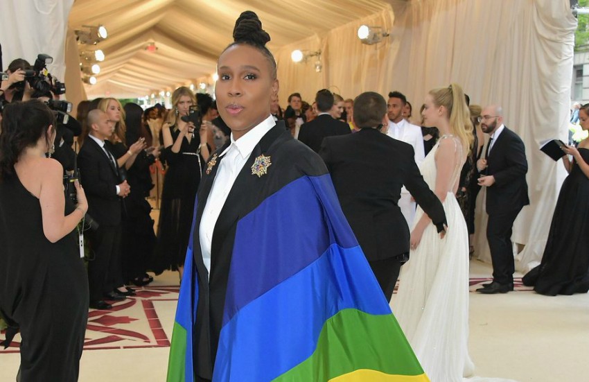 Lena waithe stands on the red carpet with a rainbow flag draped over her shoulders