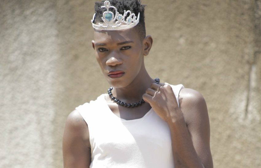 a woman with short hear wearing a silver tiara and white dress standing in front of a concrete wall