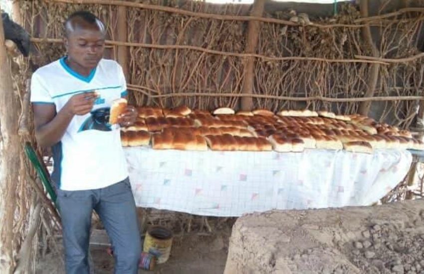 a man stands in front of a long table that is covered in loaves of bread