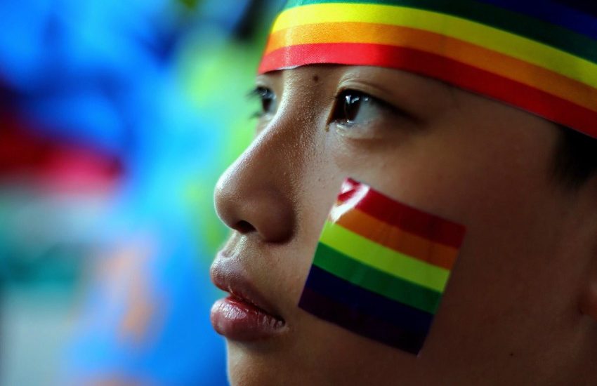 close up of a young person's face (their profile), they have a rainbow sticker on their face and a rainbow headband on their head.