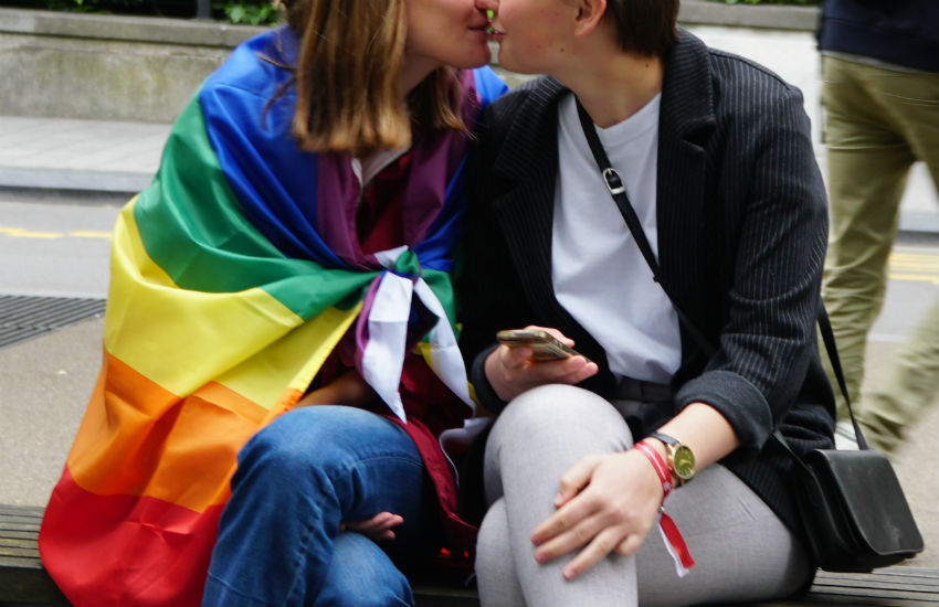 Woman wearing a rainbow flag kisses woman