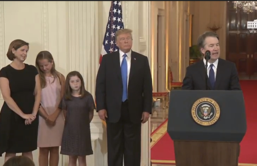 a man standing behind a lectern, donald trump is next to him. next to trump are two young girls and their mother who is wearing a black dress