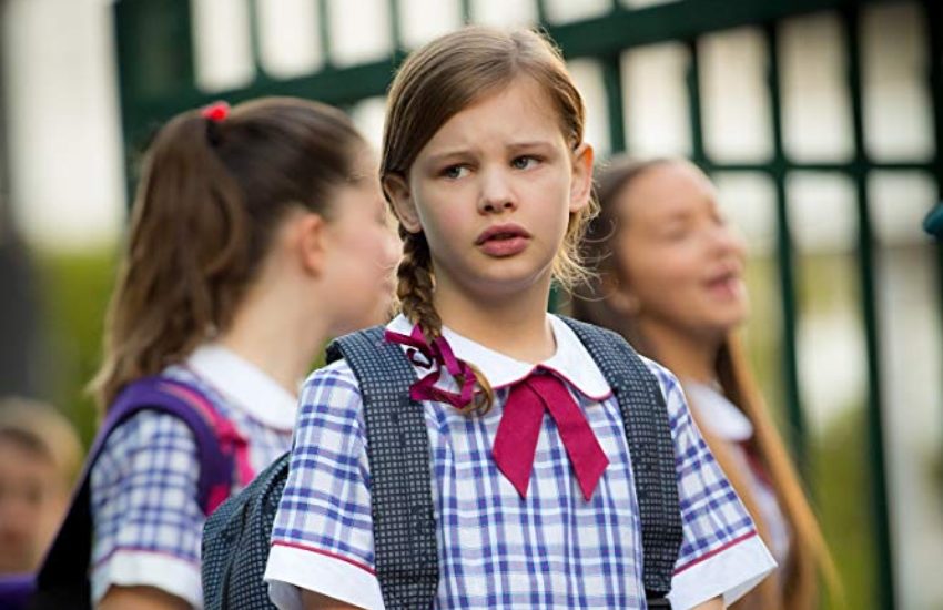 a still shot from a film showing a girl in a school uniform standing outside the school gates looking distressed
