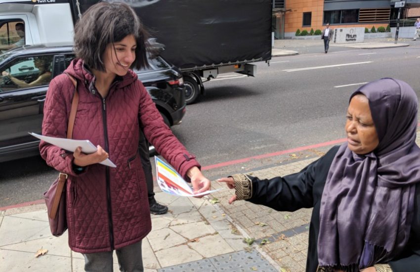 a woman handing out a leaflet to a shorter woman wearing a hijab