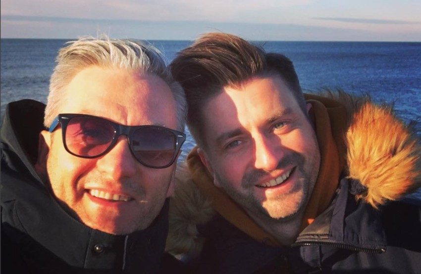 Robert Biedroń and Krzysztof Śmiszek smiling in a selfie. it is a close up shot they are both wearing big winter jackets and there is a body of water behind them