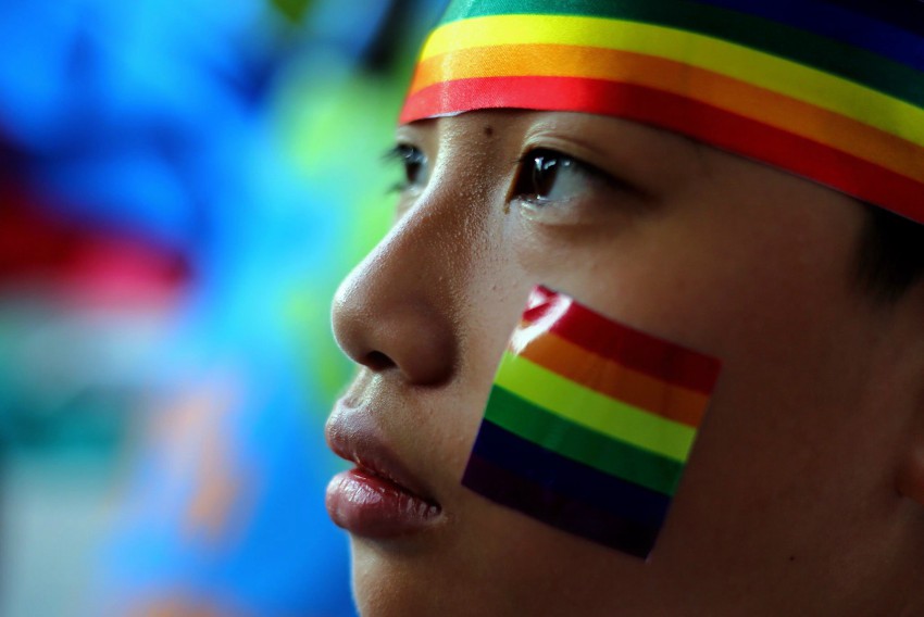 close up of a young person's face (their profile), they have a rainbow sticker on their face and a rainbow headband on their head.